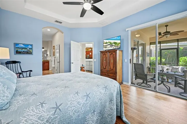 Bedroom featuring a tray ceiling, connected bathroom, hardwood / wood-style flooring, and ceiling fan