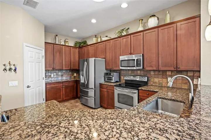 Kitchen with light tile patterned floors, dark stone counters, backsplash, stainless steel appliances, and sink