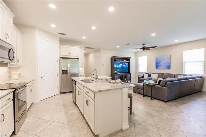 Kitchen featuring white cabinets, appliances with stainless steel finishes, a kitchen island with sink, light stone countertops, and sink