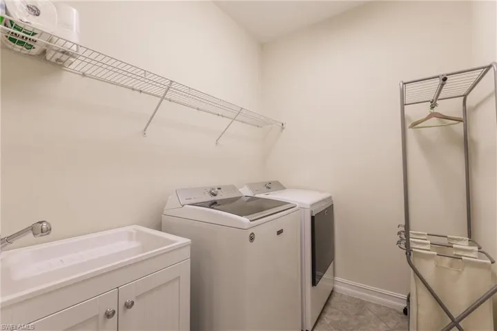 Clothes washing area with cabinets, washer and dryer, sink, and light tile patterned floors