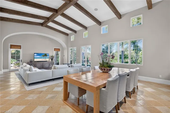 Dining area with beam ceiling, high vaulted ceiling, and stone tile flooring