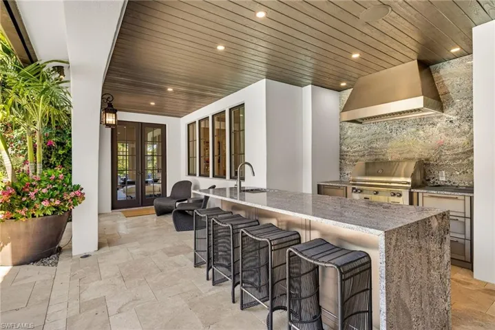 Kitchen with french doors, custom exhaust hood, stone tile floors, light stone countertops, and a kitchen breakfast bar
