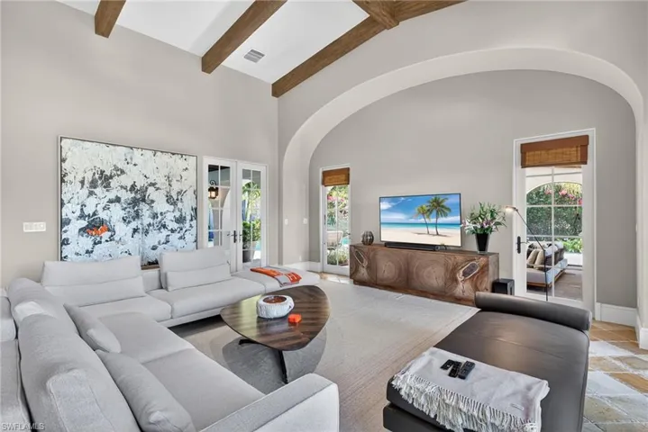 Living area featuring high vaulted ceiling, beamed ceiling, arched walkways, and stone tile floors