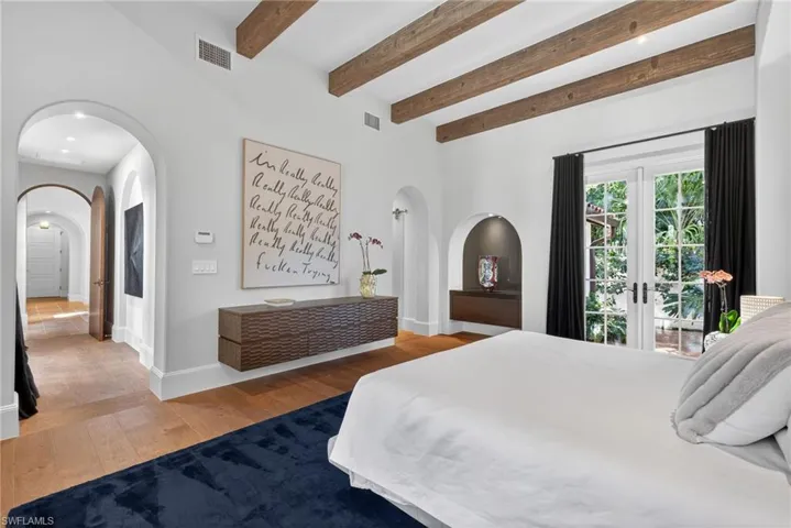 Bedroom featuring light wood-style flooring, beam ceiling, arched walkways, and french doors