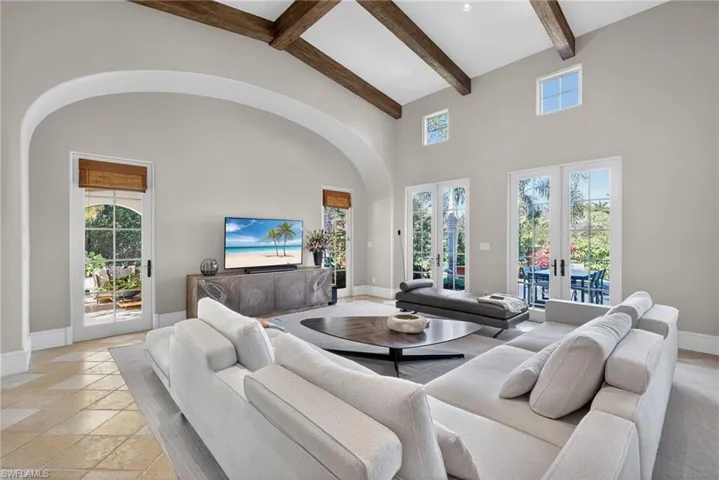 Living area with a high ceiling, arched walkways, beam ceiling, stone tile floors, and french doors