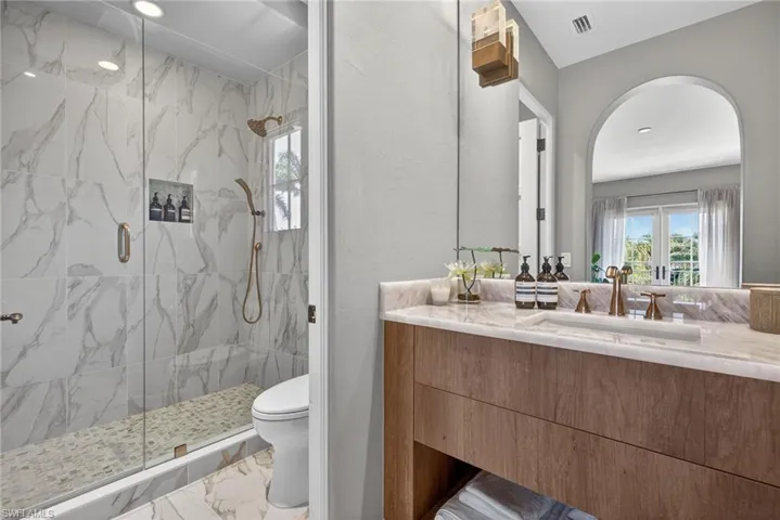 Full bathroom with a marble finish shower, light marble finish flooring, vanity, and plenty of natural light