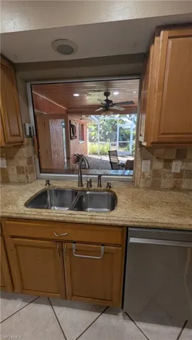 Kitchen with brown cabinets, stainless steel dishwasher, light stone countertops, tasteful backsplash, and ceiling fan
