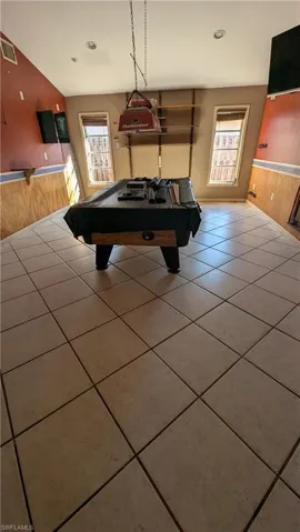 Playroom featuring a wainscoted wall, wood walls, pool table, tile patterned flooring, and lofted ceiling