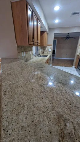 Kitchen with backsplash, a ceiling fan, light stone counters, and brown cabinets