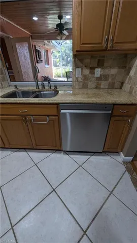 Kitchen with brown cabinetry, dishwasher, ceiling fan, and light stone counters