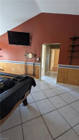 Playroom with billiards table, wainscoting, light tile patterned flooring, lofted ceiling, and wooden walls