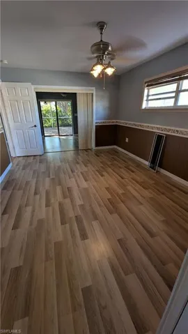 Empty room with wood finished floors, a ceiling fan, and a wainscoted wall