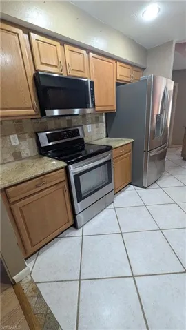 Kitchen with appliances with stainless steel finishes, backsplash, light stone countertops, and brown cabinetry