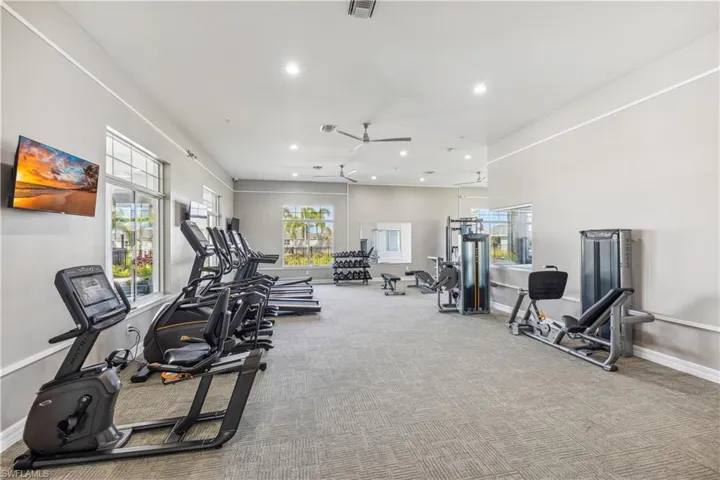 Fitness center featuring a variety of exercise equipment, carpeted flooring, and windows with views of palm trees