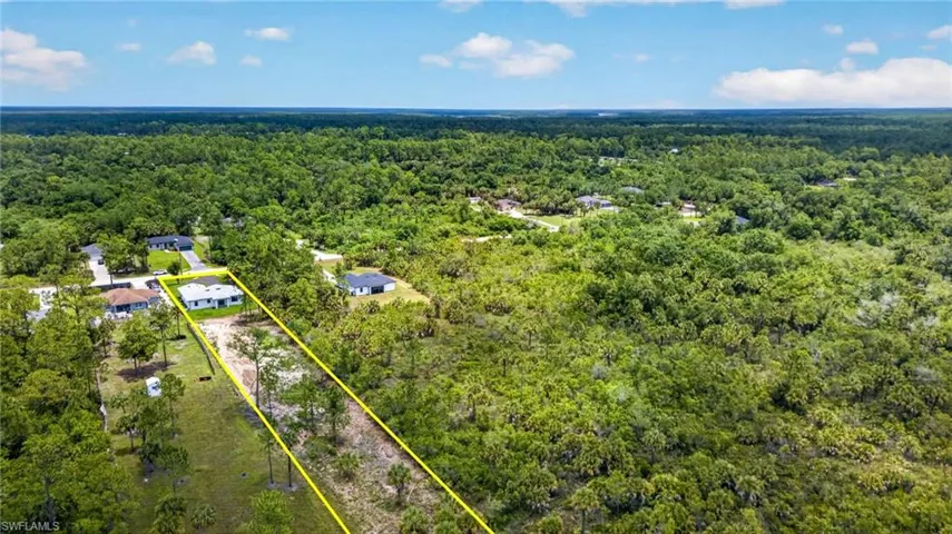 Expansive land parcel featuring a residential structure, mature trees, and a surrounding natural landscape