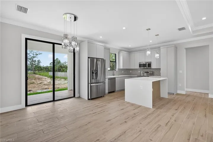Open-concept living area featuring wood-finish flooring, a contemporary kitchen with stainless steel appliances, a center island, and a decorative pendant light fixture, with crown molding throughout