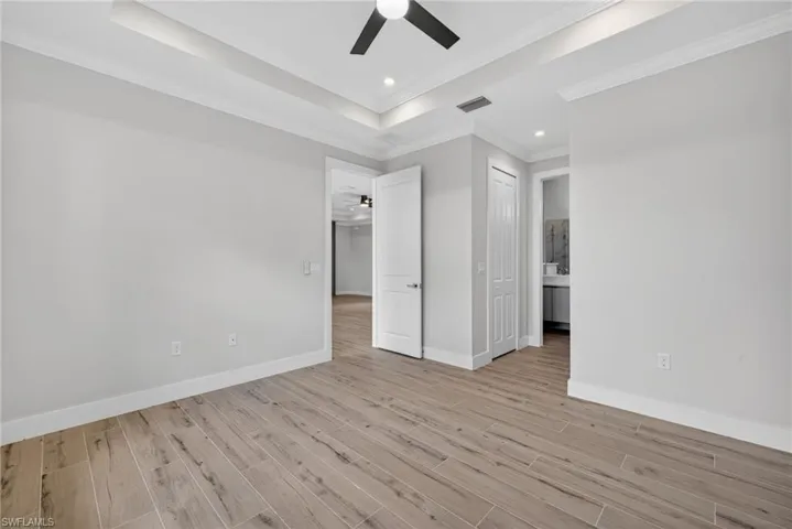Spacious room with wood-finish flooring, tray ceiling, recessed lighting, and a contemporary ceiling fan