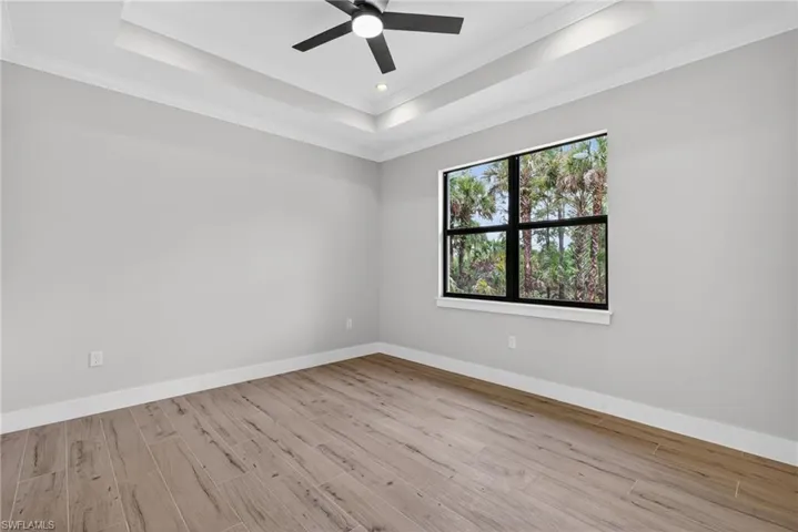Spacious room featuring wood-finish flooring, a tray ceiling with recessed lighting, and a contemporary ceiling fan