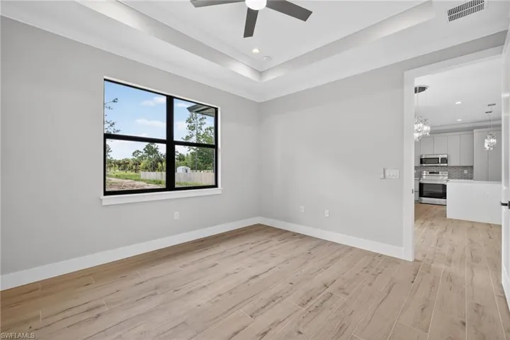 Spacious room featuring light wood-finish flooring, a tray ceiling with recessed lighting and a ceiling fan, and a large window with black framing