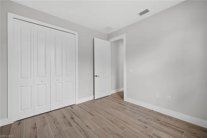 Spacious interior room featuring wood-finish flooring, light gray wall paint, and white trim
