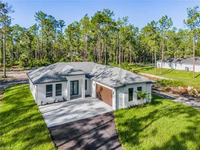View of front facade featuring roof with shingles, a front lawn, driveway, an attached garage, and stucco siding