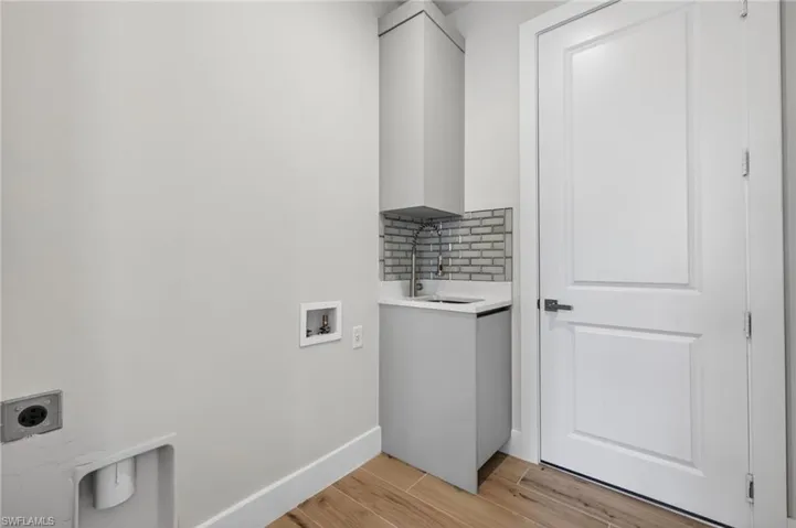 Utility room featuring a built-in sink with a tile backsplash, gray cabinetry, wood-finish flooring, and a paneled interior door