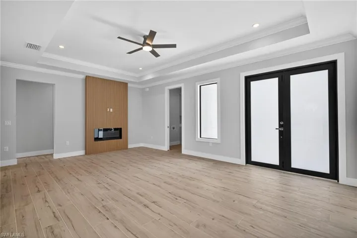 Spacious interior room featuring wood-finish flooring, a modern built-in fireplace with wood paneling, a tray ceiling with recessed lighting, and a ceiling fan