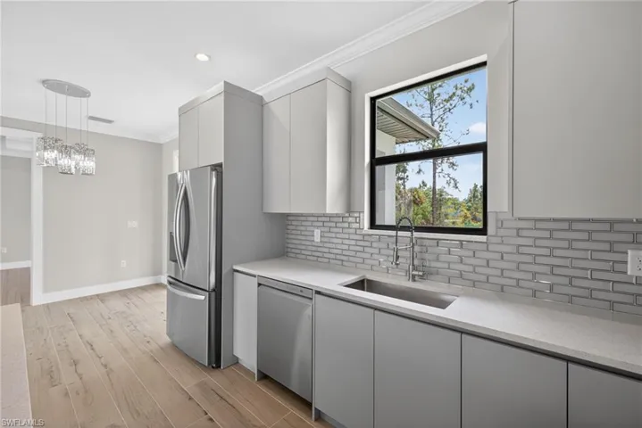 Contemporary kitchen featuring light gray flat-panel cabinetry, stainless steel appliances, a subway tile backsplash, and light-toned countertops