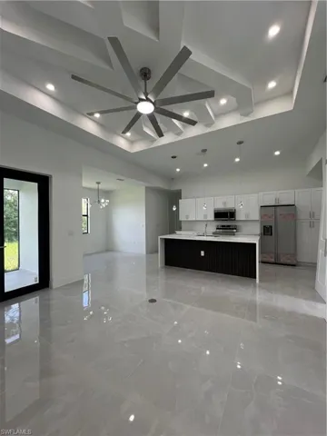 Unfurnished living room with ceiling fan, recessed lighting, a chandelier, light marble finish floors, and a tray ceiling