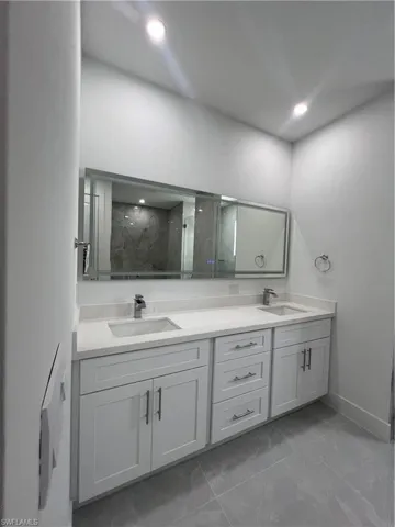 Full bath featuring double vanity, a marble finish shower, and marble look tile flooring