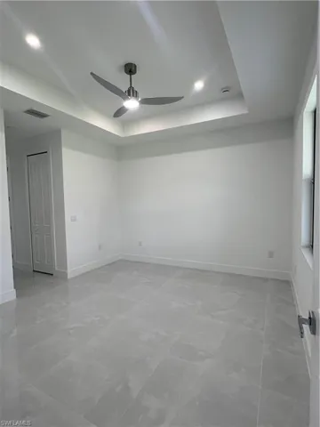 Empty room featuring a tray ceiling, a ceiling fan, light marble finish flooring, and recessed lighting