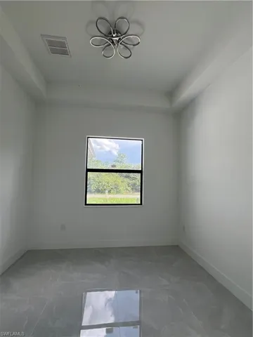 Empty room with a chandelier, a tray ceiling, and marble look tile flooring