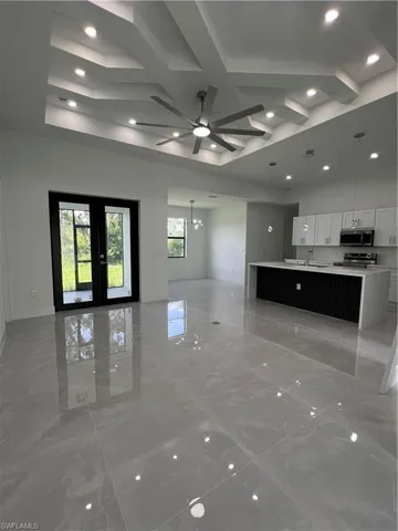 Unfurnished living room featuring light marble finish floors, a chandelier, ceiling fan, recessed lighting, and coffered ceiling