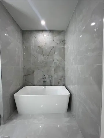 Full bathroom featuring tile walls, marble tiled flooring, and a soaking tub
