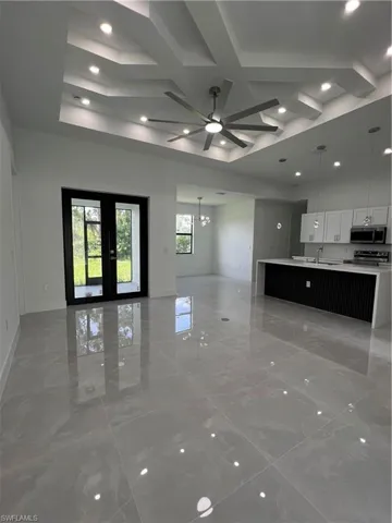 Unfurnished living room with light marble finish flooring, ceiling fan, a chandelier, and coffered ceiling