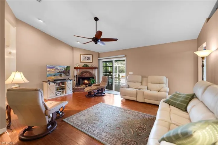 Living area featuring wood flooring, a ceiling fan, a brick fireplace, and lofted ceiling