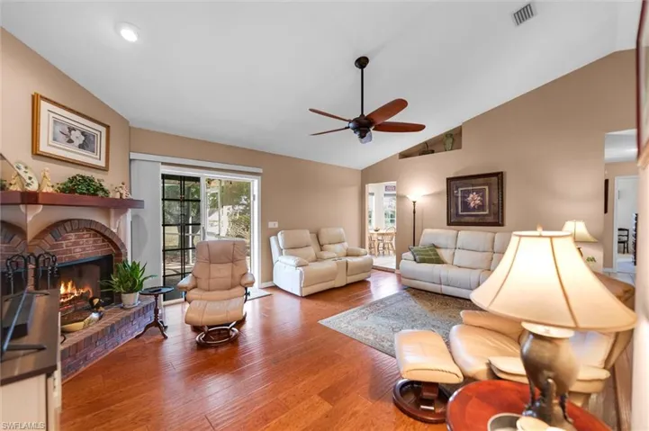 Living room featuring vaulted ceiling, ceiling fan, a brick fireplace, and wood flooring