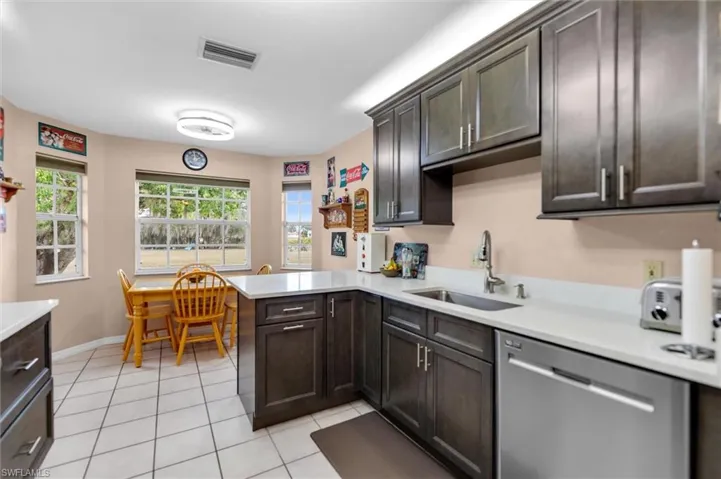 Kitchen with dishwasher, dark wood finish cabinetry, light tile patterned floors, a peninsula, and light quarts countertops
