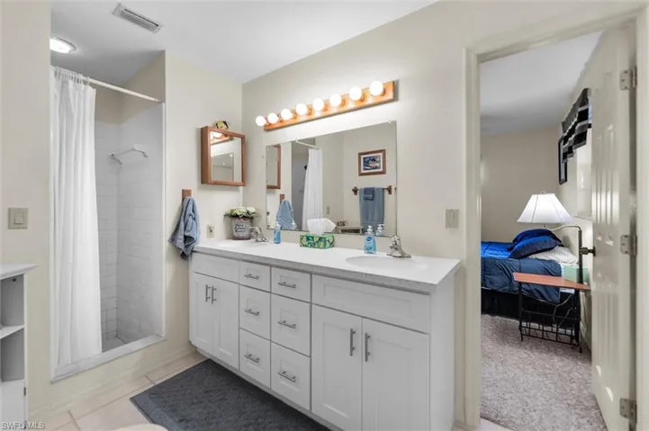 Full jack and jill bathroom with ensuite bathroom, double vanity, a stall shower, and light tile patterned floors