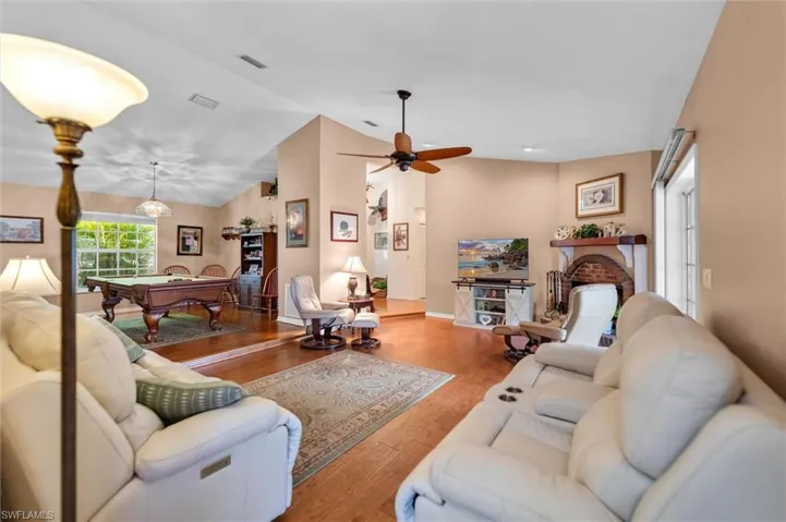 Living room featuring lofted ceiling, wood floors, a ceiling fan, a brick fireplace, and billiards