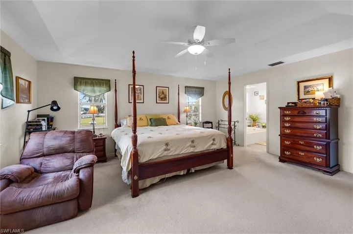 Carpeted bedroom featuring multiple windows, a ceiling fan, and ensuite bath