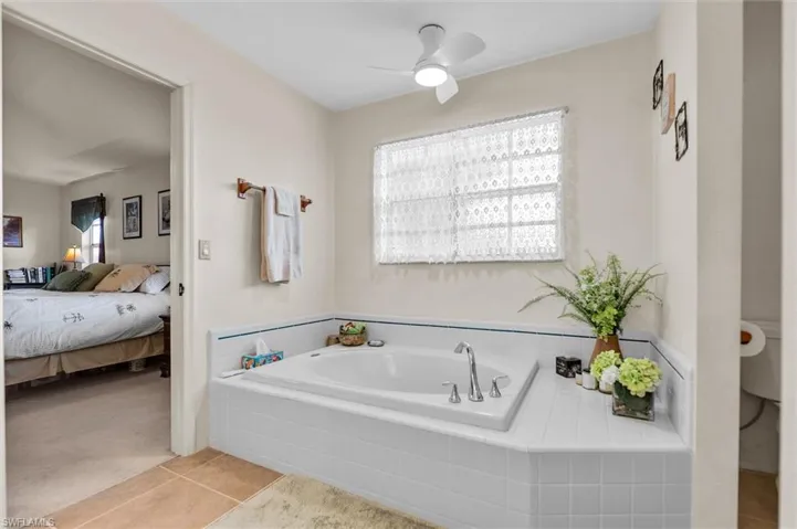 Ensuite bathroom with a garden tub, light tile patterned floors, ceiling fan, and light carpet