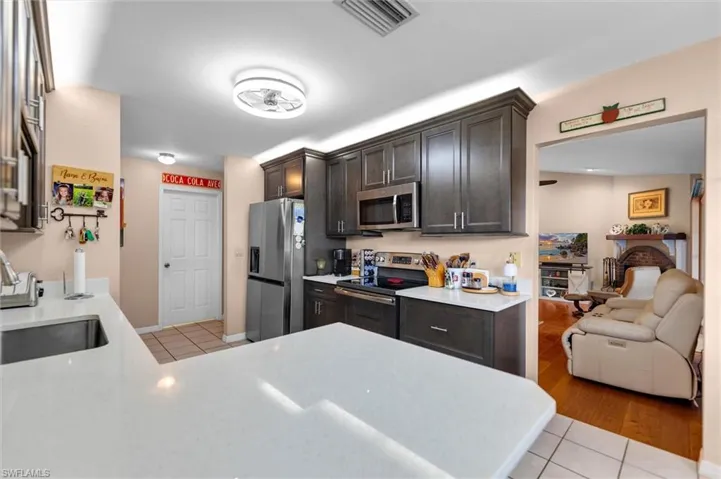 Kitchen with stainless steel appliances, light tile patterned floors, a peninsula, dark wood finish cabinets, and light quarts counters