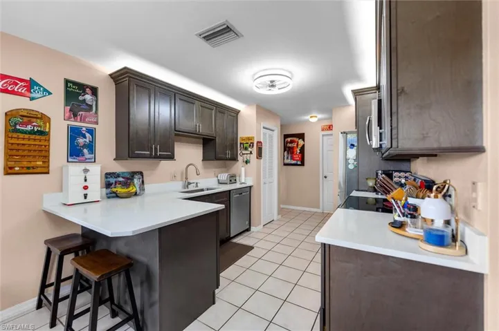 Kitchen featuring a peninsula, a kitchen bar, dark wood finish cabinets, quarts countertops, light tile patterned floors, and stainless steel appliances