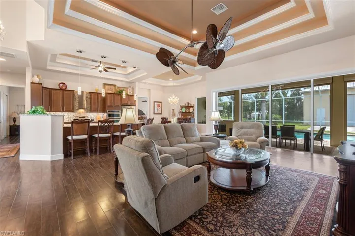 Living room featuring dark hardwood / wood-style flooring, ceiling fan, a raised ceiling, and ornamental molding