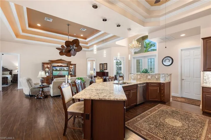 Kitchen with sink, dark hardwood / wood-style floors, ceiling fan with notable chandelier, and a raised ceiling