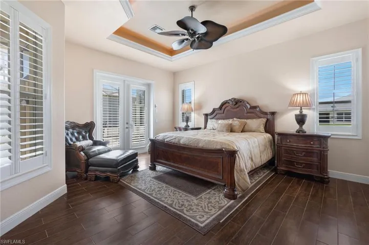 Bedroom featuring ceiling fan, dark hardwood / wood-style flooring, a tray ceiling, and multiple windows