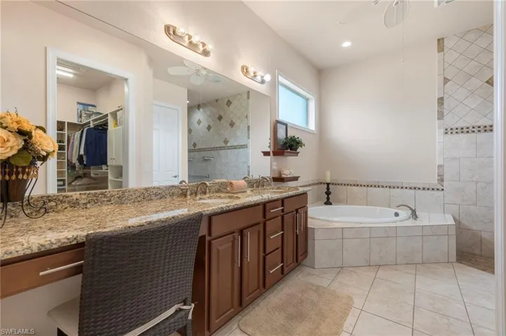 Bathroom with a relaxing tiled tub, vanity, tile patterned flooring, and ceiling fan