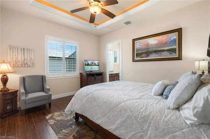 Bedroom featuring dark hardwood / wood-style flooring, connected bathroom, ceiling fan, and a raised ceiling