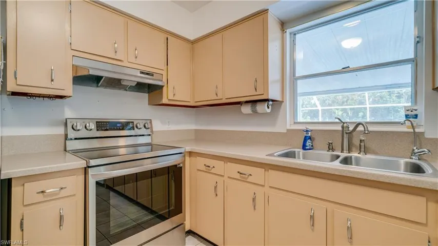 Kitchen with cream cabinets, sink, and stainless steel range with electric stovetop